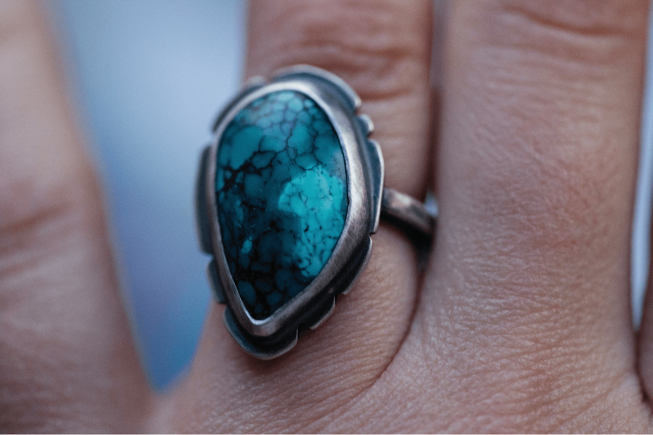 close up image of a hand wearing a silver ring with a large turquoise gem