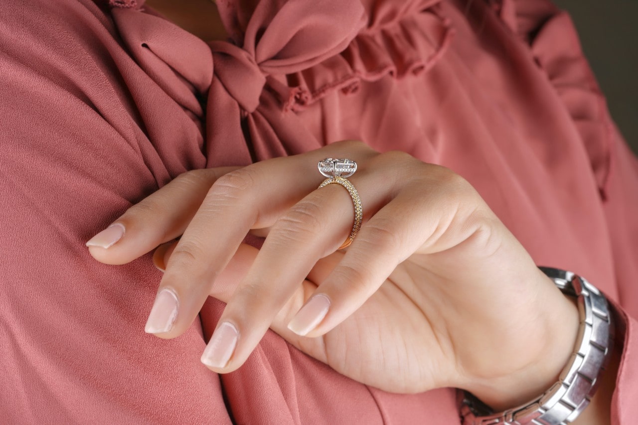 a woman in a pink blouse wearing a gold engagement ring and a silver watch.