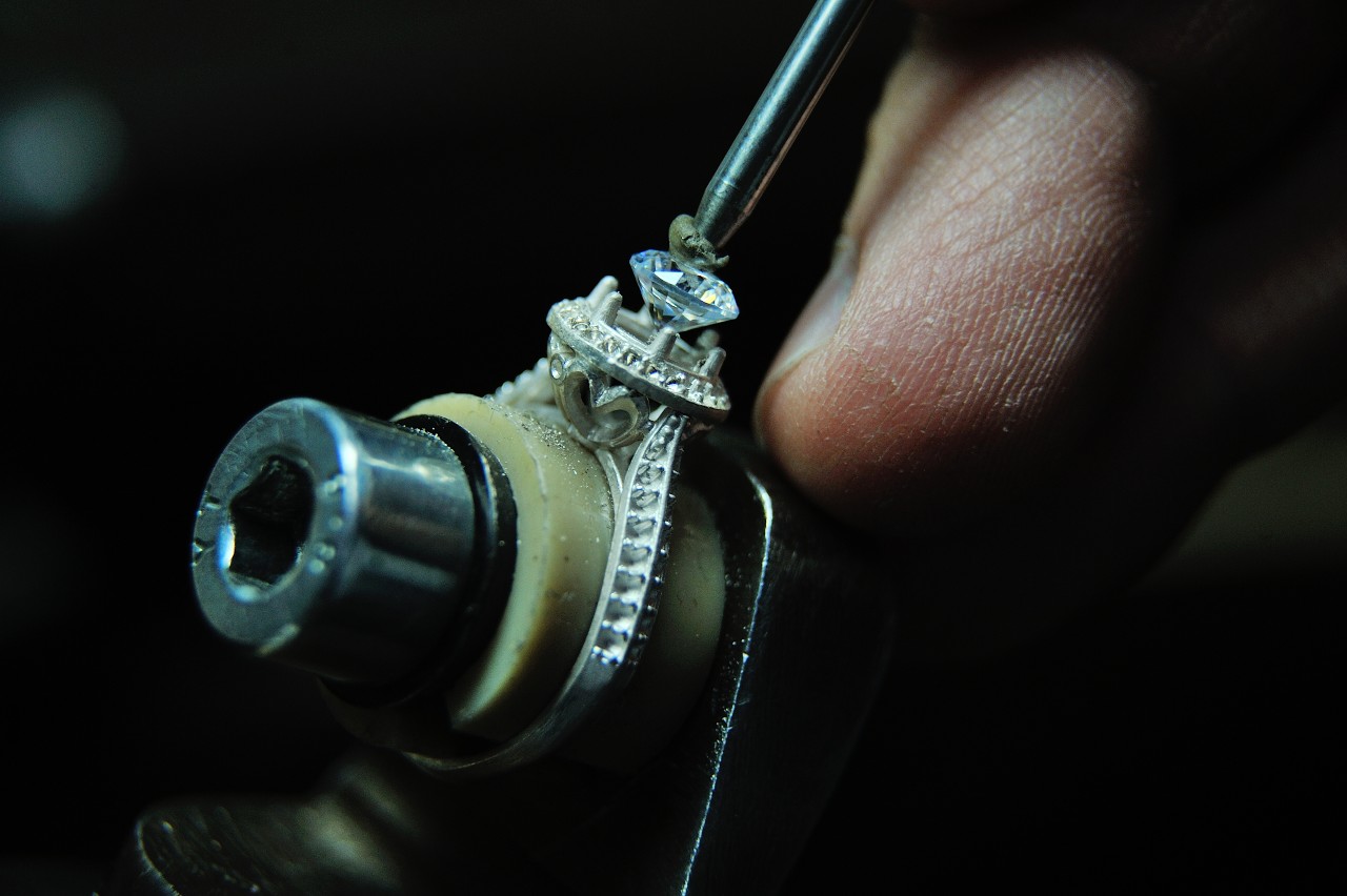 A jeweler places a diamond in a halo engagement ring setting.