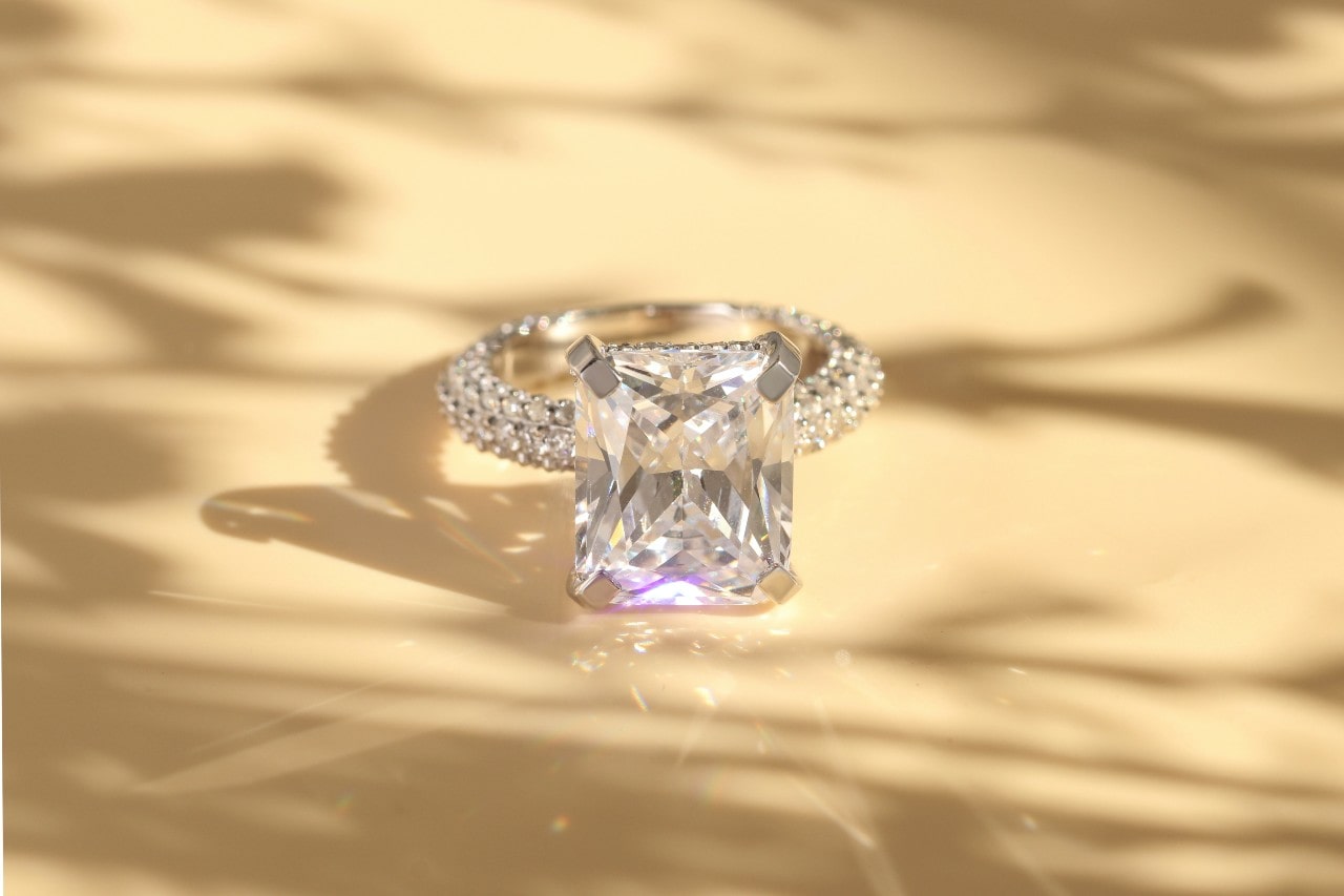 an emerald cut engagement ring with a maximalist silhouette against a beige background