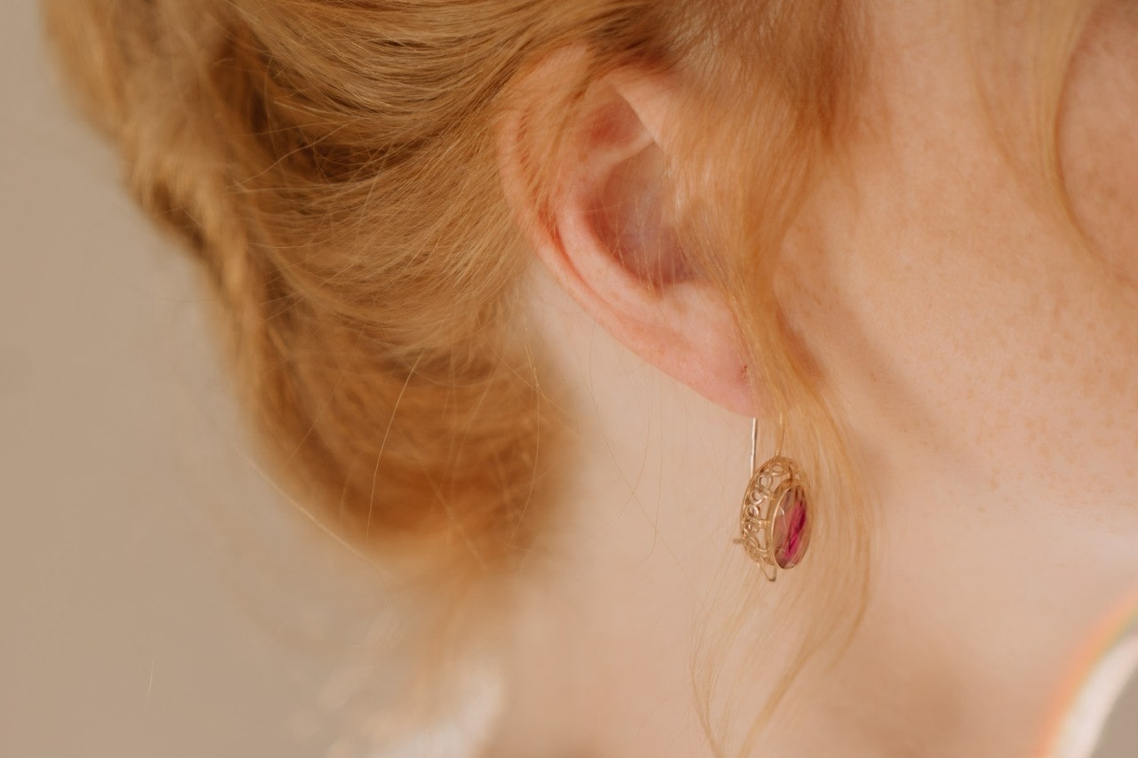 close up image of a woman wearing a gold earring featuring a spinel gem