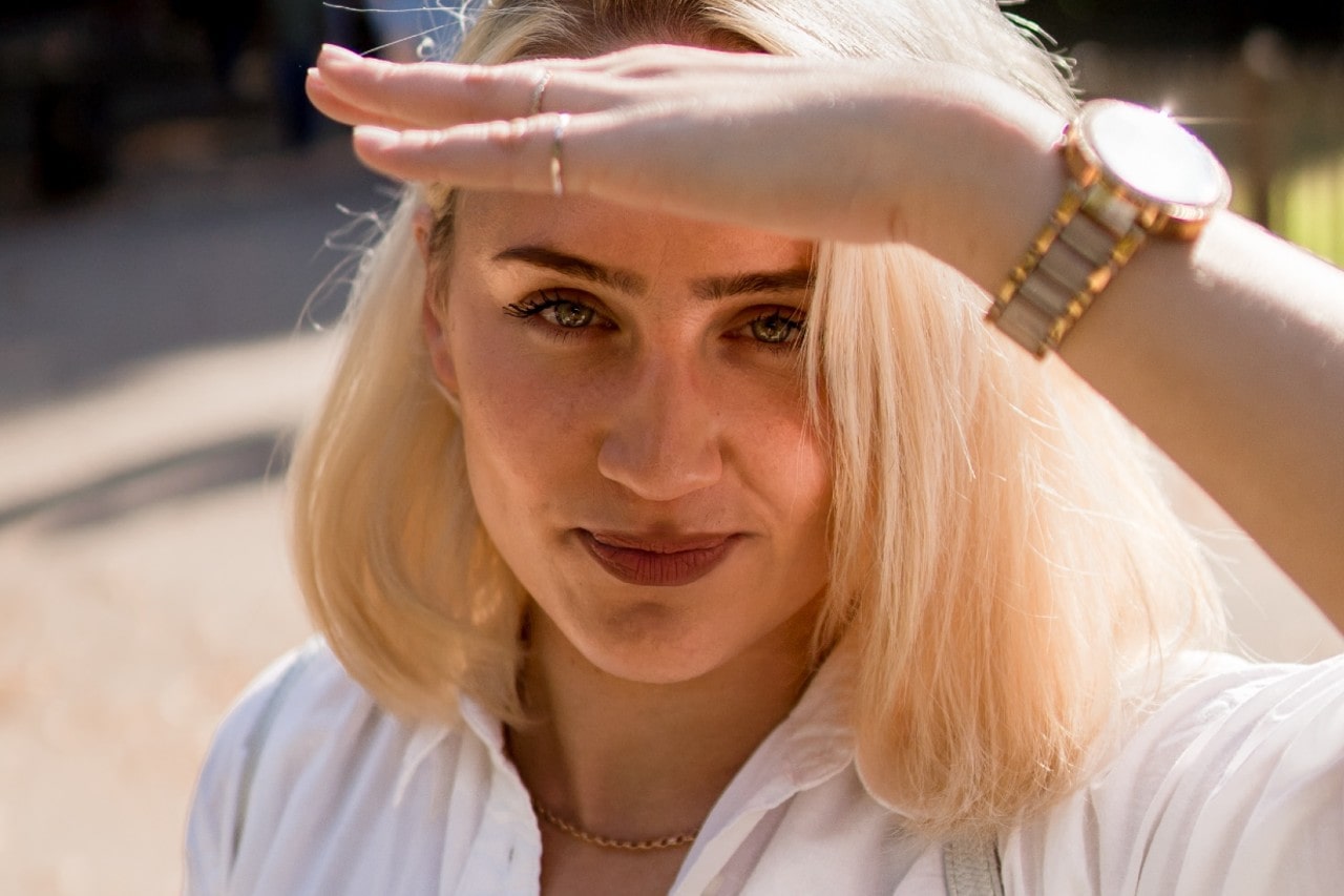 A close-up of a woman shielding her eyes from the sun and wearing a mixed metal watch.
