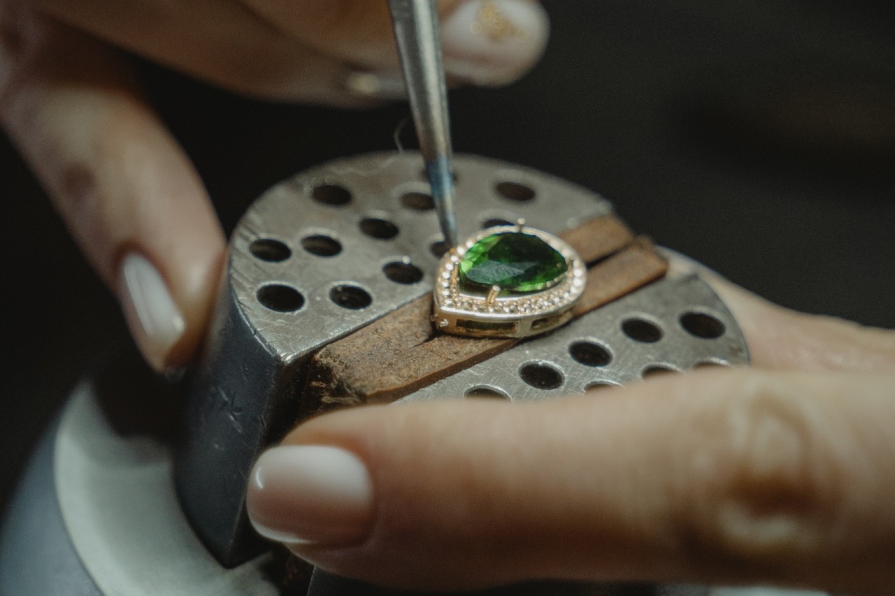 A close-up of a jeweler crafted a pendant with a green center gemstone.