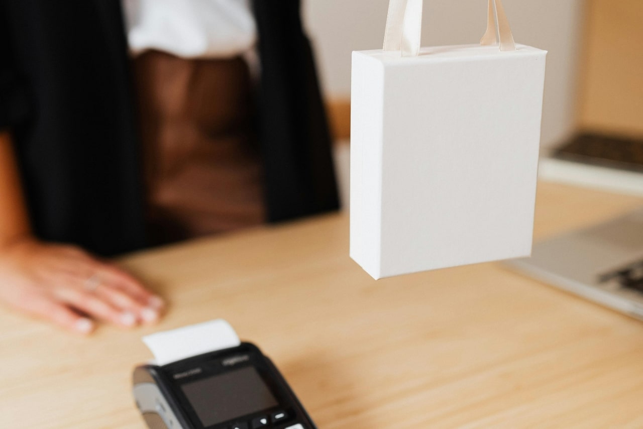 A close-up of a person standing at a counter handing over a white gift bag