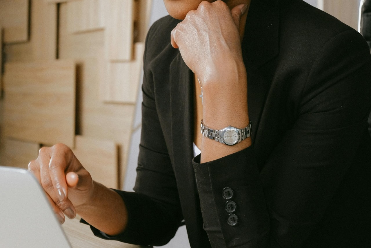 A close-up of a woman working on a laptop wearing a small silver-toned watch.