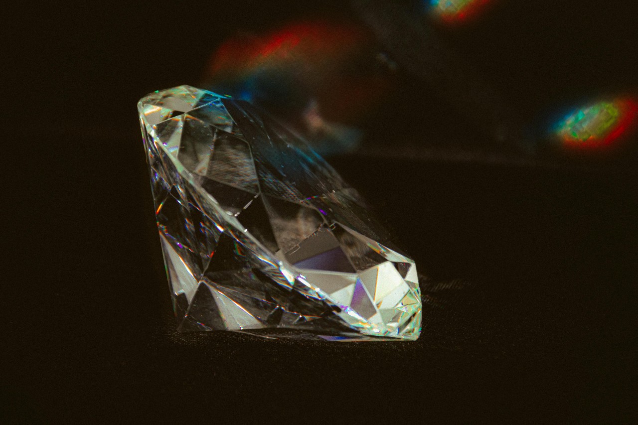 A close-up of a sparkling diamond on a black surface, showcasing its intricate facets.