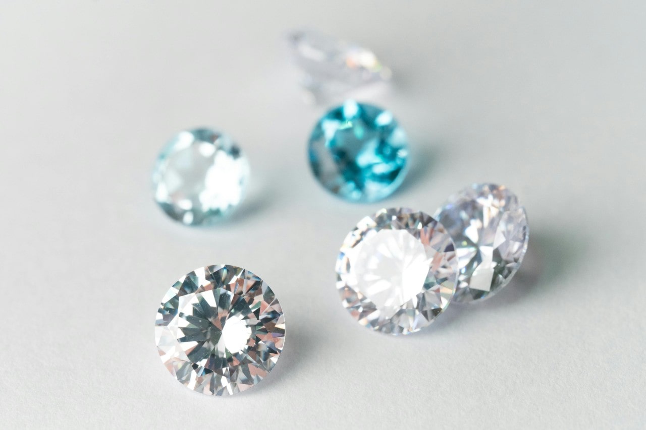 A close-up of round-cut colorless and blue diamonds sparkling on a textured white surface.