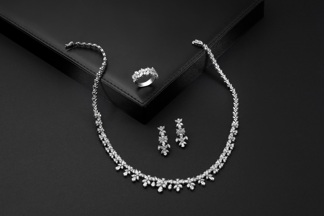 A matching diamond necklace, drop earrings, and fashion ring sits on a black surface.
