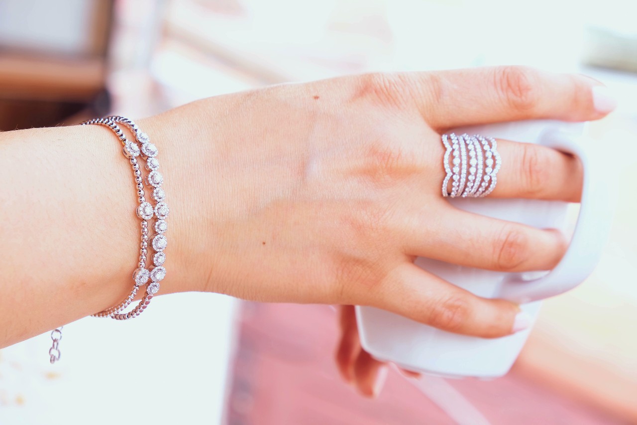 A woman’s hand holding a coffee mug while wearing diamond rings and bracelets.
