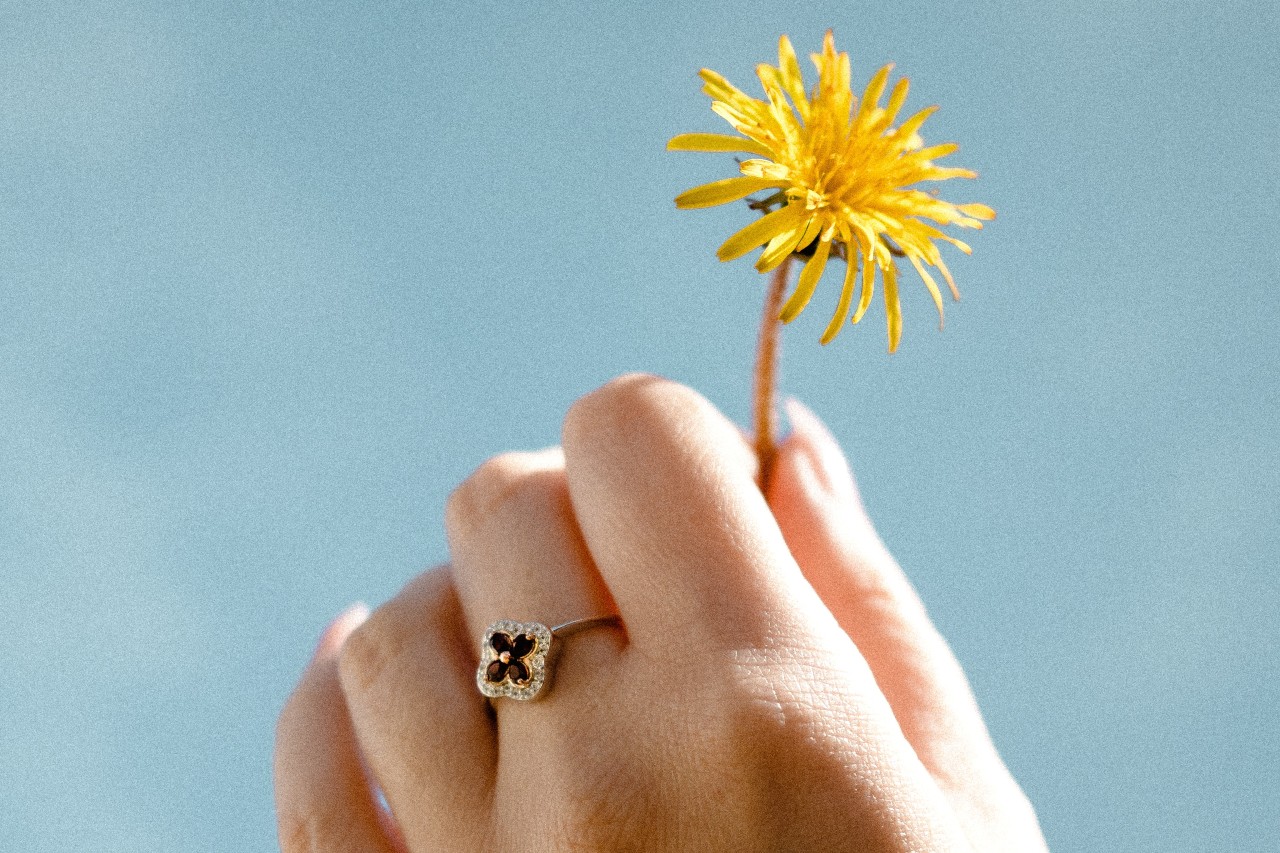 close up image of a hand holding a dandelion and wearing a floral fashion ring