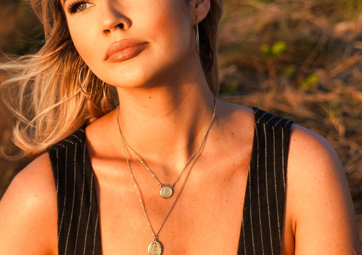 A woman in the sunlight wears two coin necklaces of different lengths.