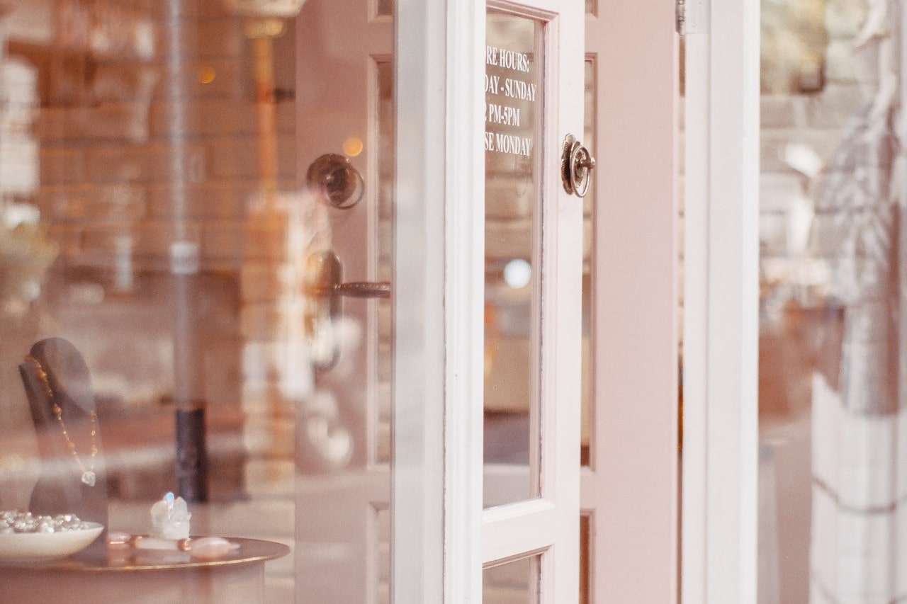 Storefront with a pink door partially open, revealing a cozy interior with jewelry displays.