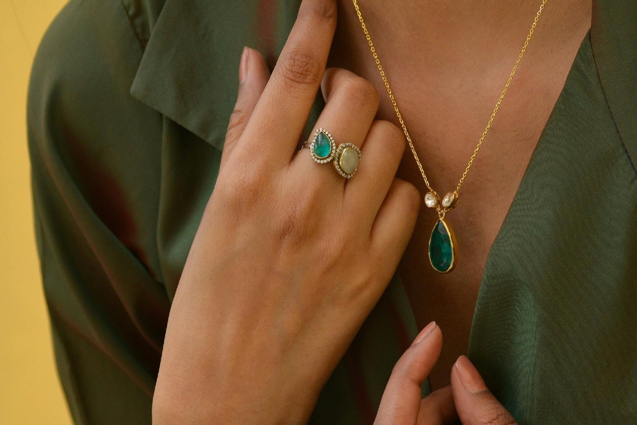 Close up of a person in a green blouse flaunting a teardrop green gemstone pendant and two stone rings.
