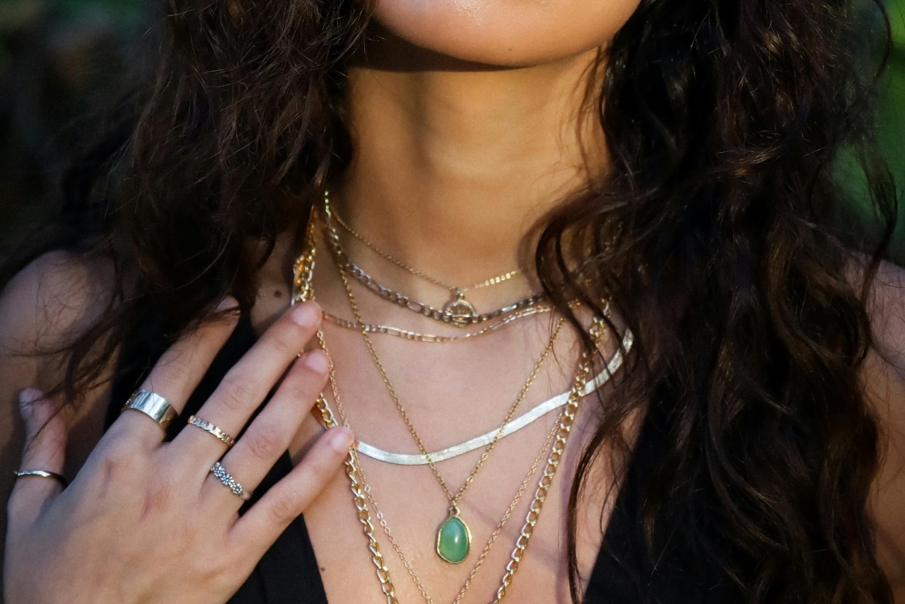 A close-up image of a woman’s neckline adorned with a number of layered gold necklaces