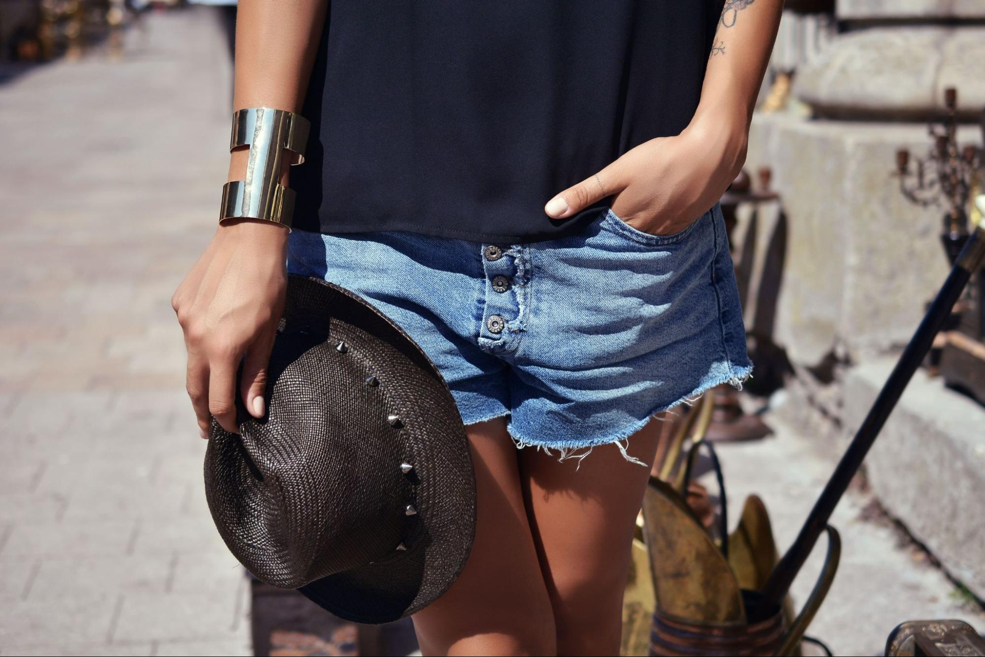 A woman wearing a chunky bangle bracelet carries her hat as she walks down a path.