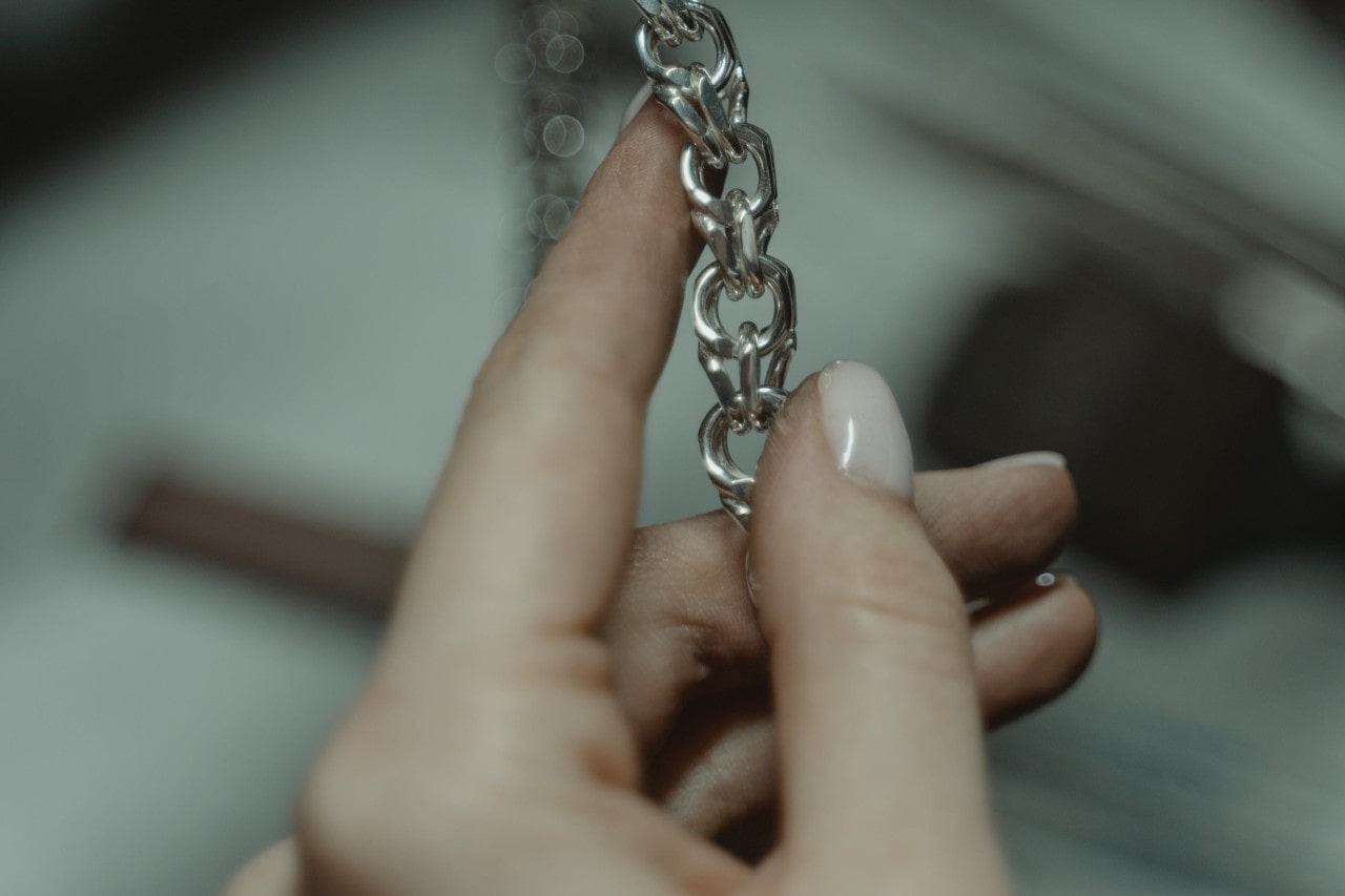 a jeweler’s hand inspecting a silver chain