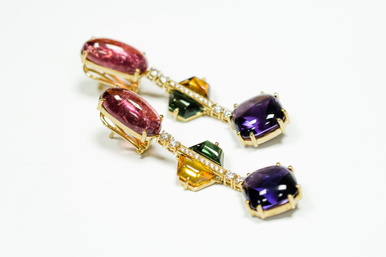 a pair of yellow gold, gemstone, and diamond earrings on a white surface