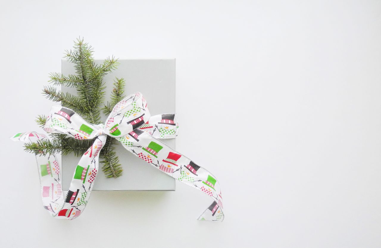 A view of a grey jewelry box decorated with a snowman ribbon and a sprig of pine.