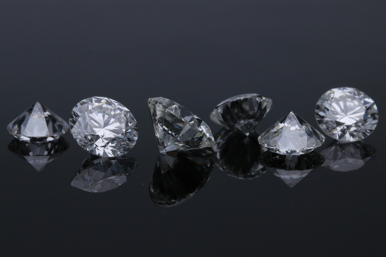 A line of six round cut diamonds on a reflective black surface.