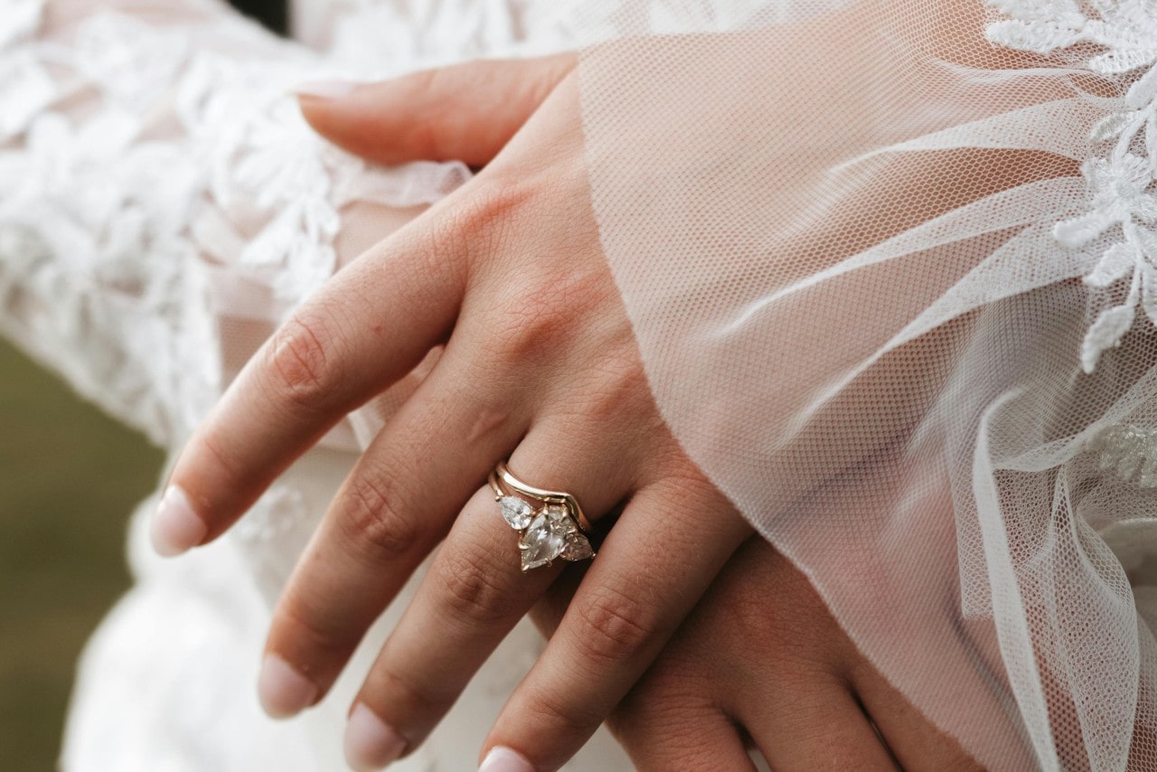 A close-up image of a bride’s hands adorned with a three stone engagement ring and matching wedding band.