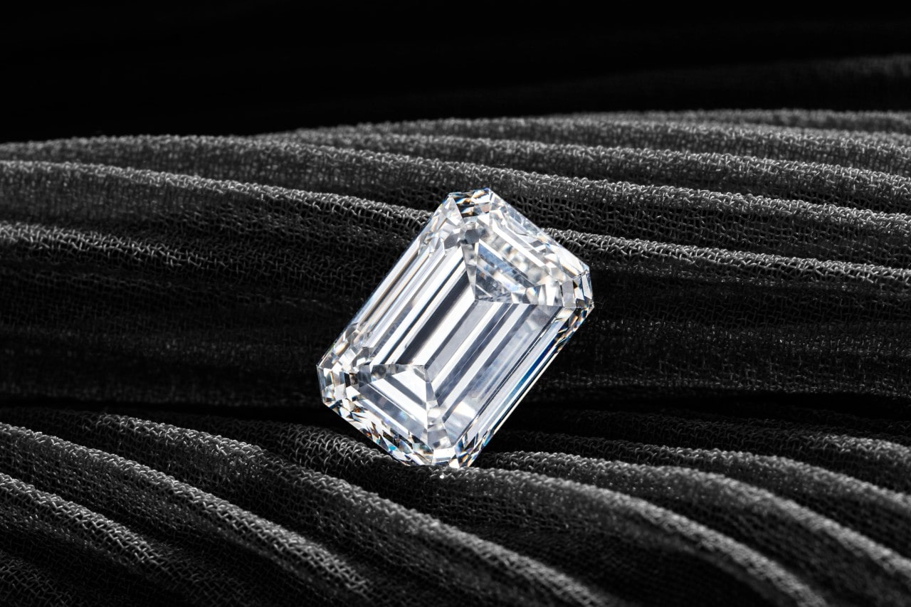 A luminous emerald cut diamond sitting on a black textured surface