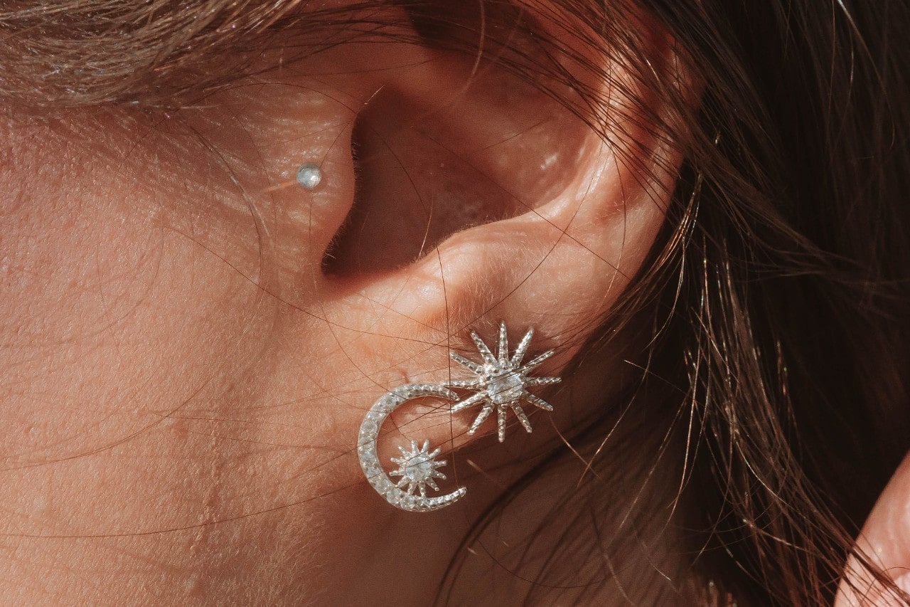a close up image of a woman’s ear wearing sun and moon earrings