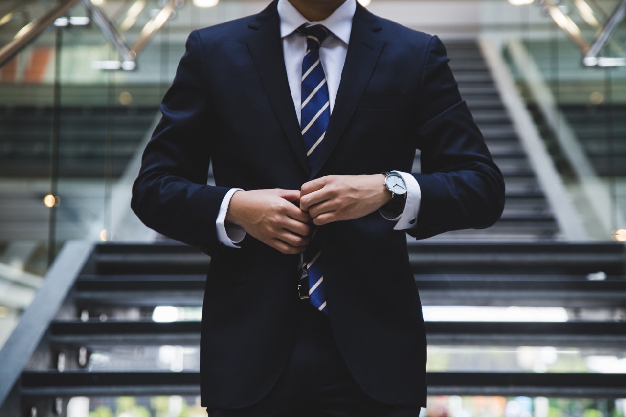 A man holding the front button on his suit and showcasing a white watch.