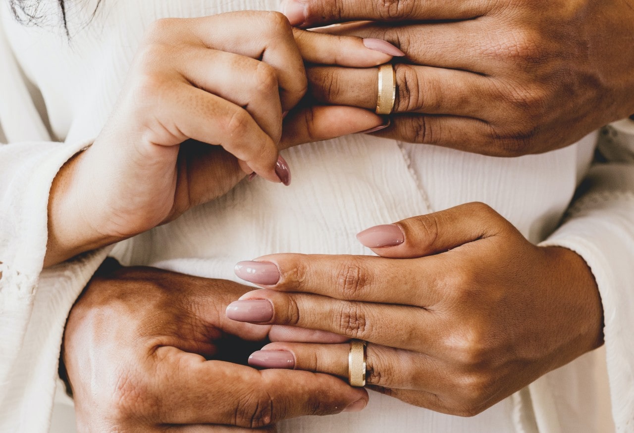 a bride and groom simultaneously placing wedding bands on each others fingers