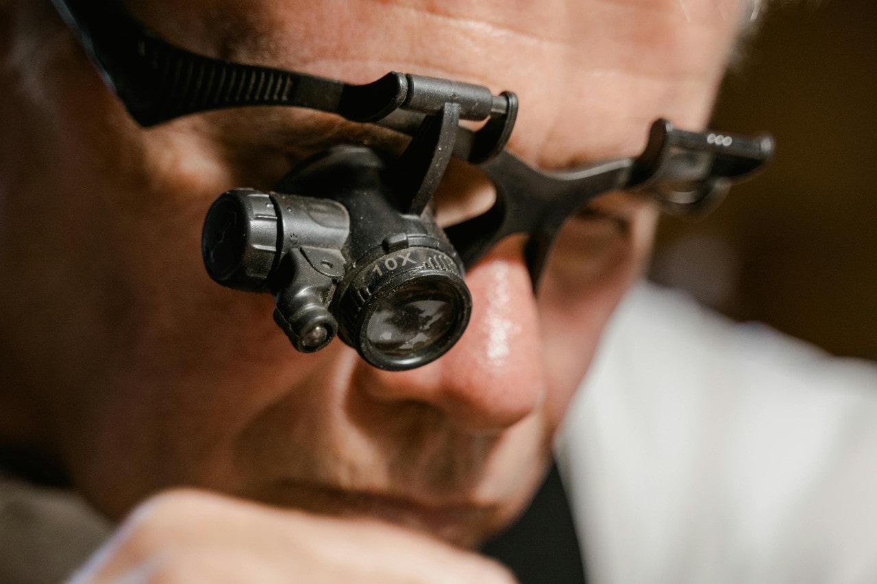 A close-up of a jeweler wearing a magnifying headset as he inspects a piece of jewelry.