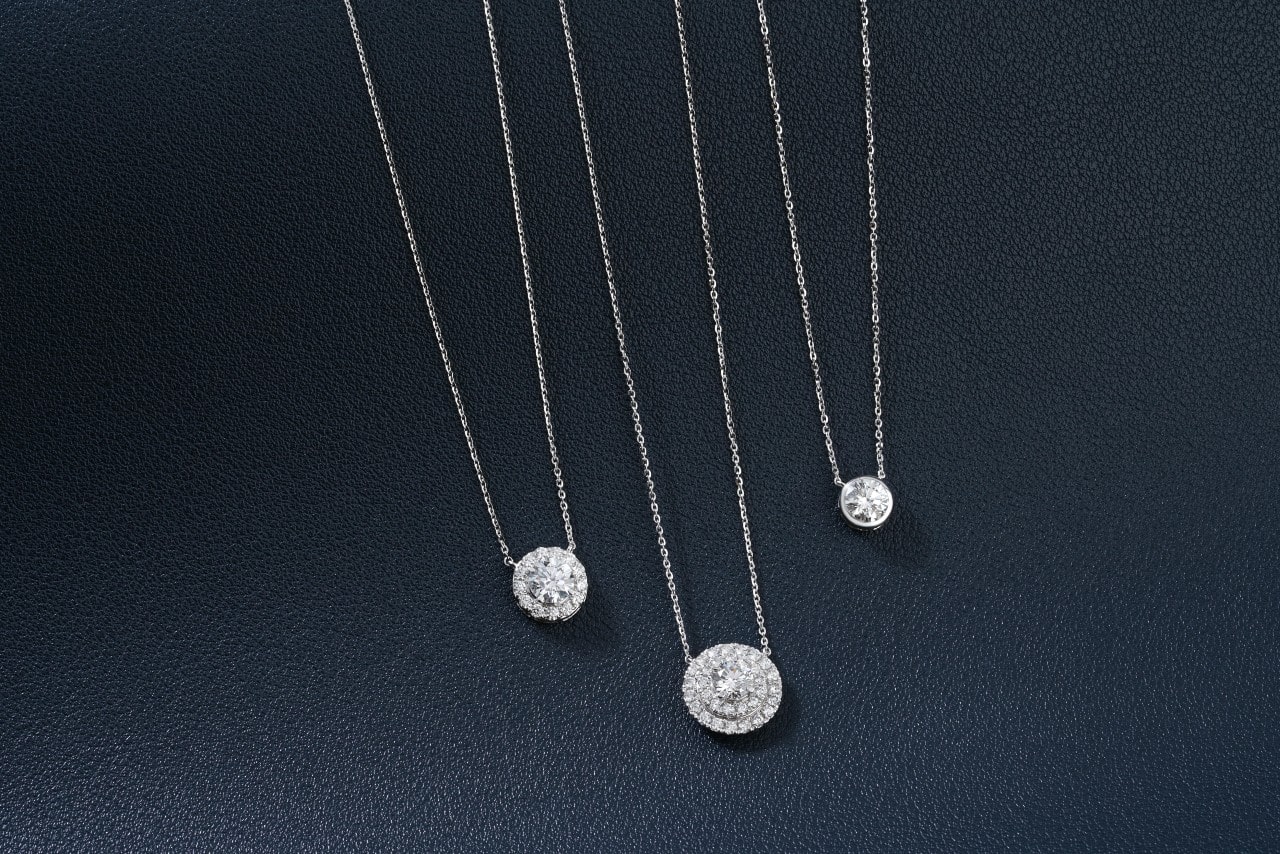 Three diamond pendant necklaces displayed against dark background.
