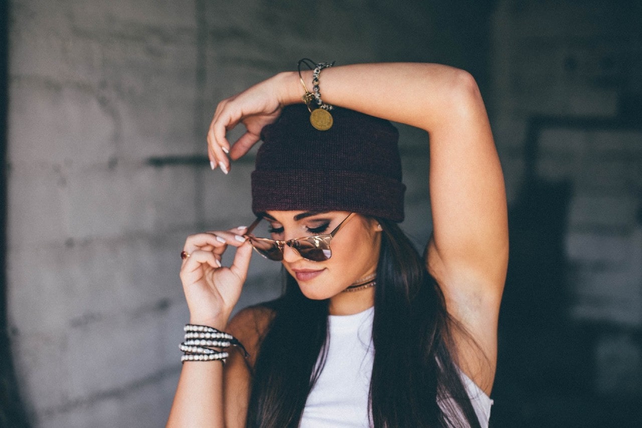 A woman wearing multiple bracelets adjusts her sunglasses.