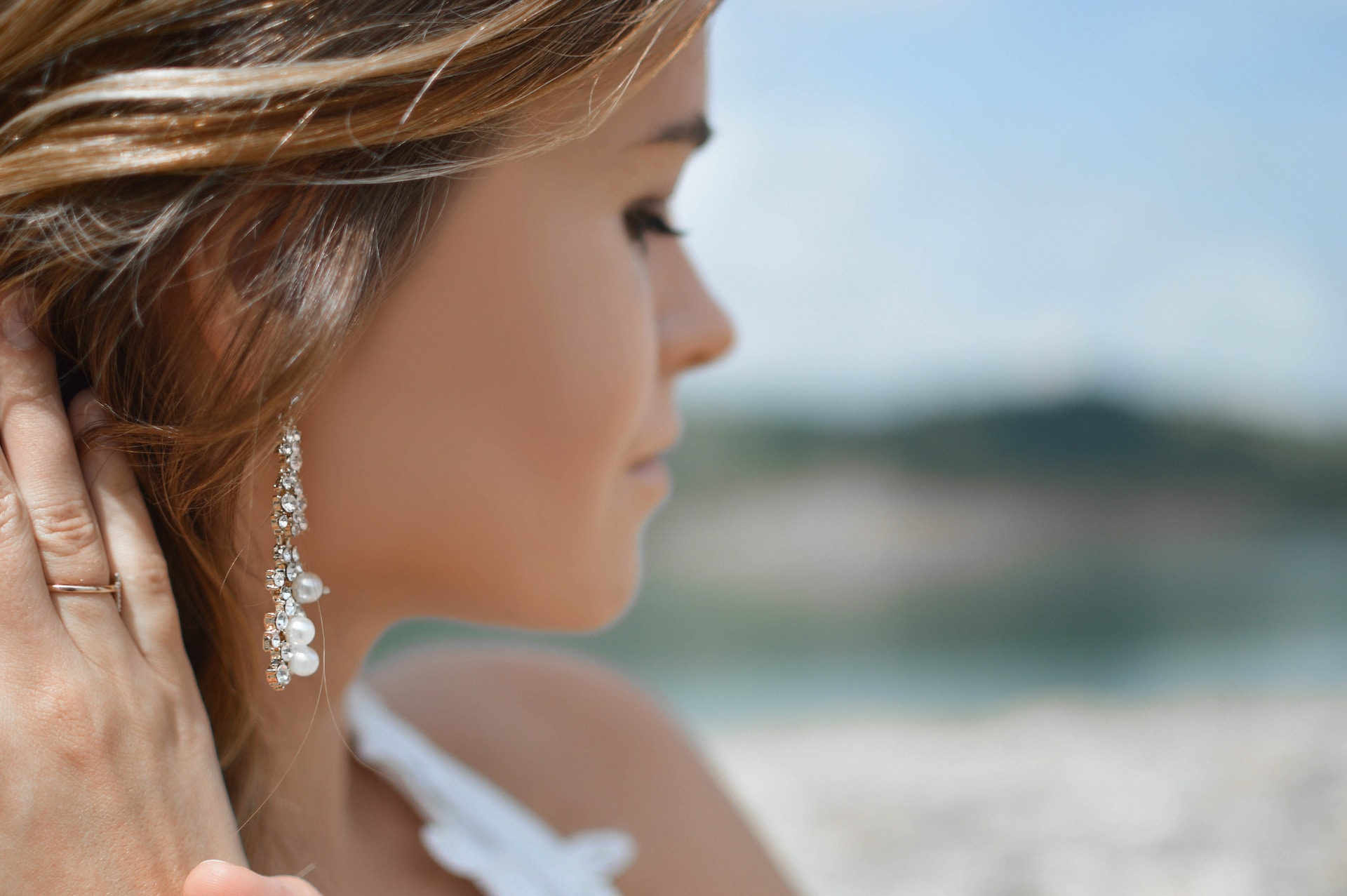 A close-up of a young woman wearing a delicate pair of diamond and pearl drop earrings.