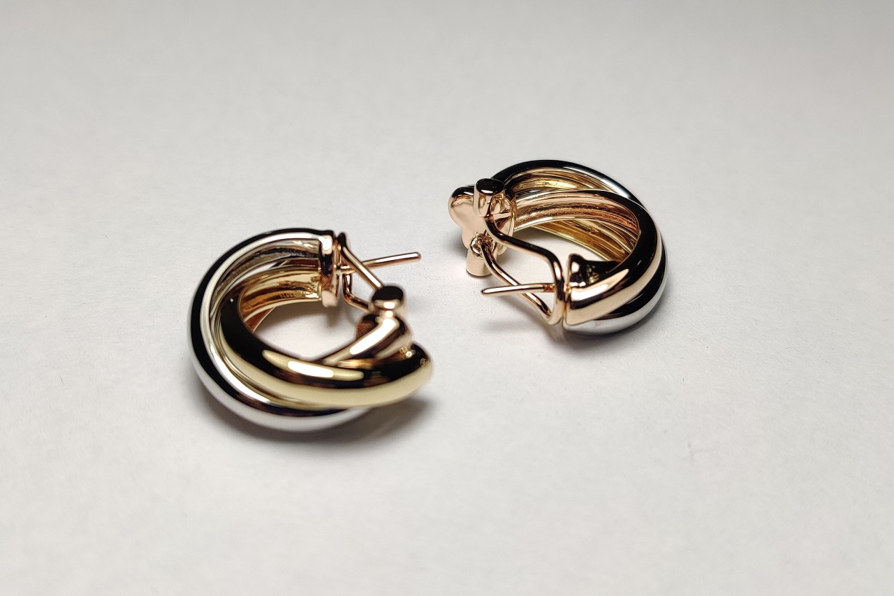 A pair of two-toned gold huggie earrings displayed on their sides on a pale backdrop.