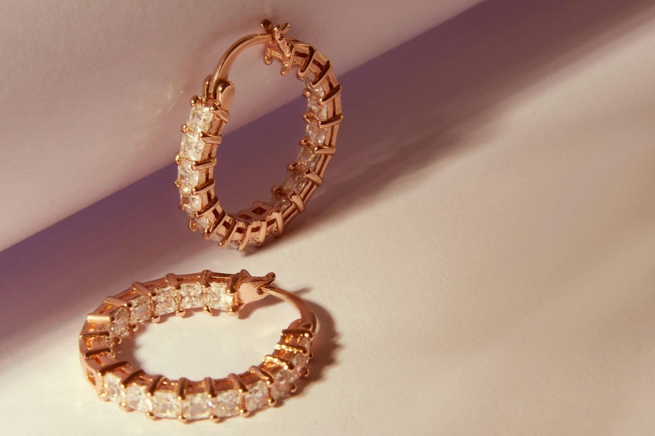 A close-up of a small pair of yellow gold diamond hoop earrings on a light backdrop.