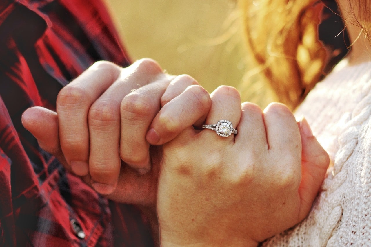 a couple with their pinkies crossed, the woman wearing a silver halo engagement ring