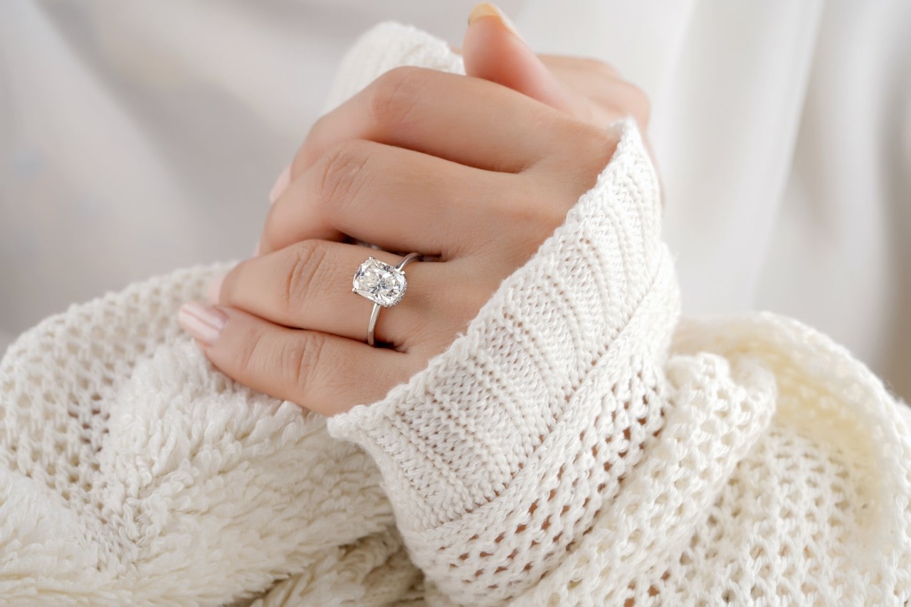 a person’s hand wearing a large diamond engagement ring and a chunky sweater.