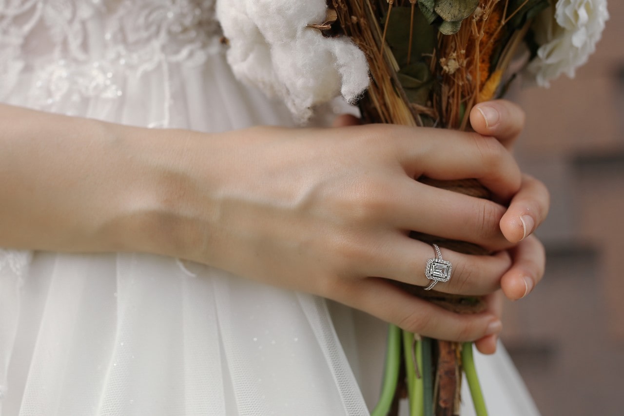 a bride holding her bouquet and wearing a large diamond halo engagement ring