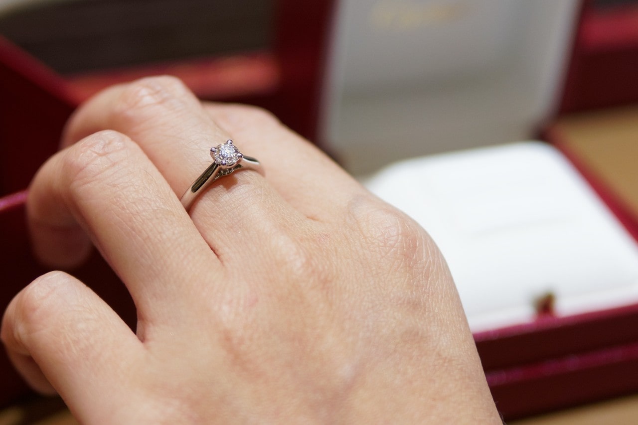 A closeup of a solitaire engagement ring on a woman’s finger.