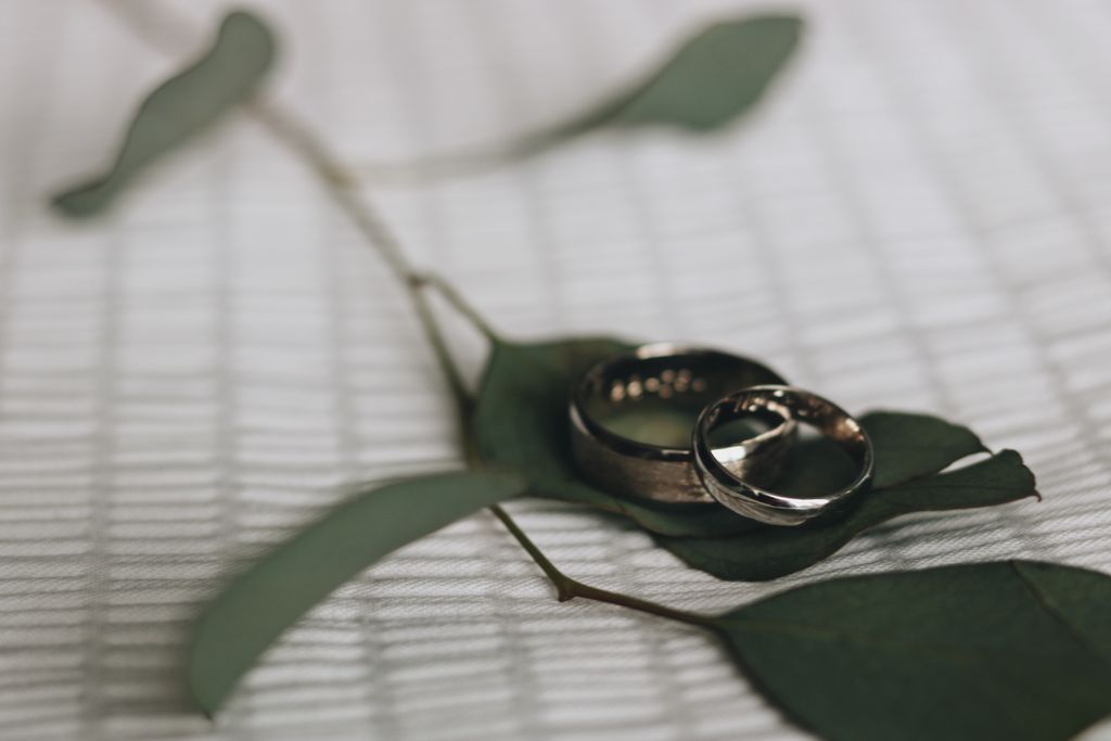 Two silver rings rest on eucalyptus leaves atop a textured white surface, conveying a serene and romantic tone with natural and elegant elements.