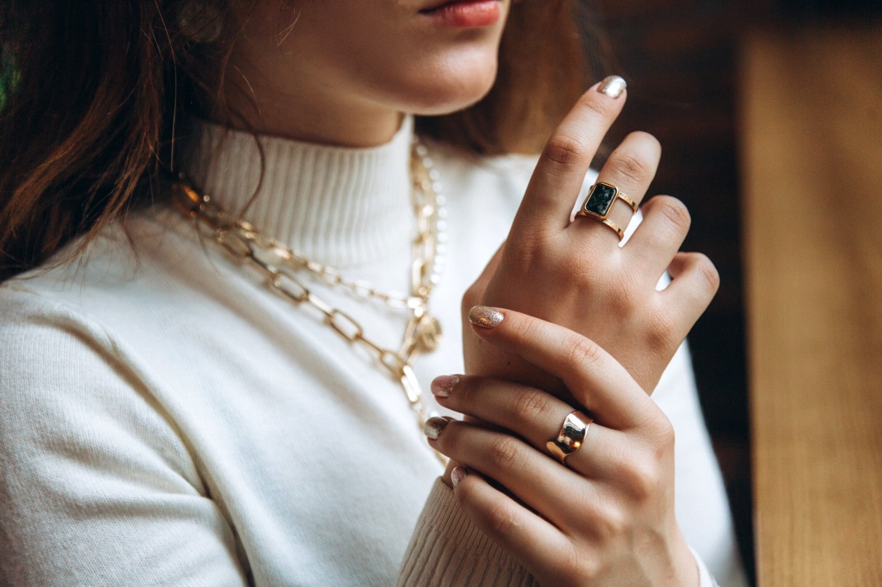 A woman in a white turtleneck, showcasing a yellow gold chain necklace and fashion rings. A woman in a white turtleneck, showcasing a yellow gold chain necklace and fashion rings.