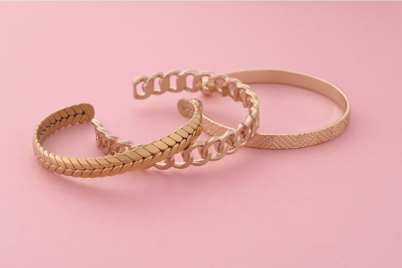 A close-up of three yellow gold bangles on a pink surface. A close-up of three yellow gold bangles on a pink surface.
