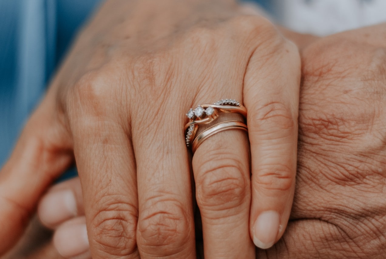 Close-up of two hands gently holding, with one wearing gold rings featuring small diamonds in an intertwined design.