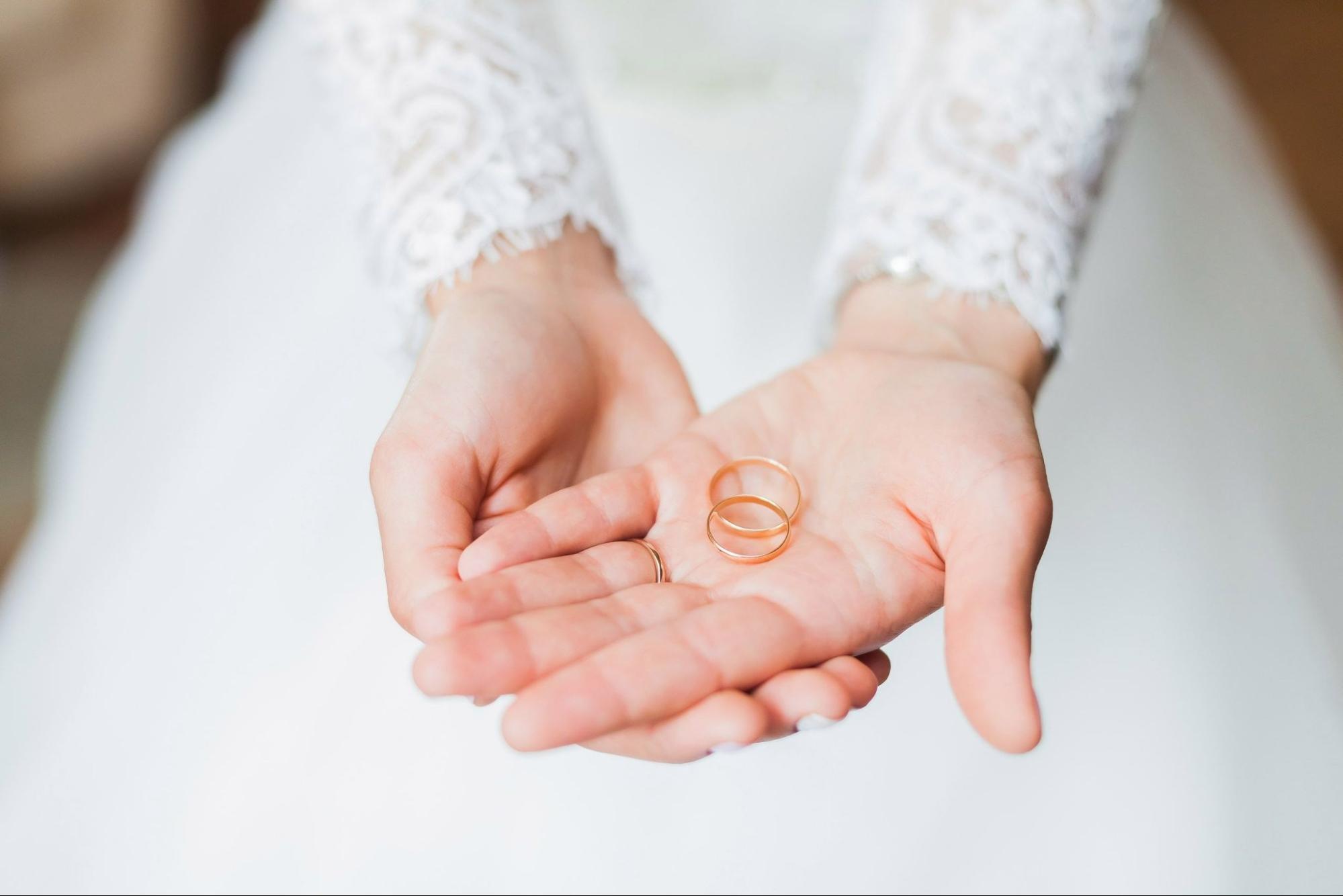 A bride holds two rose gold wedding bands in her palm.