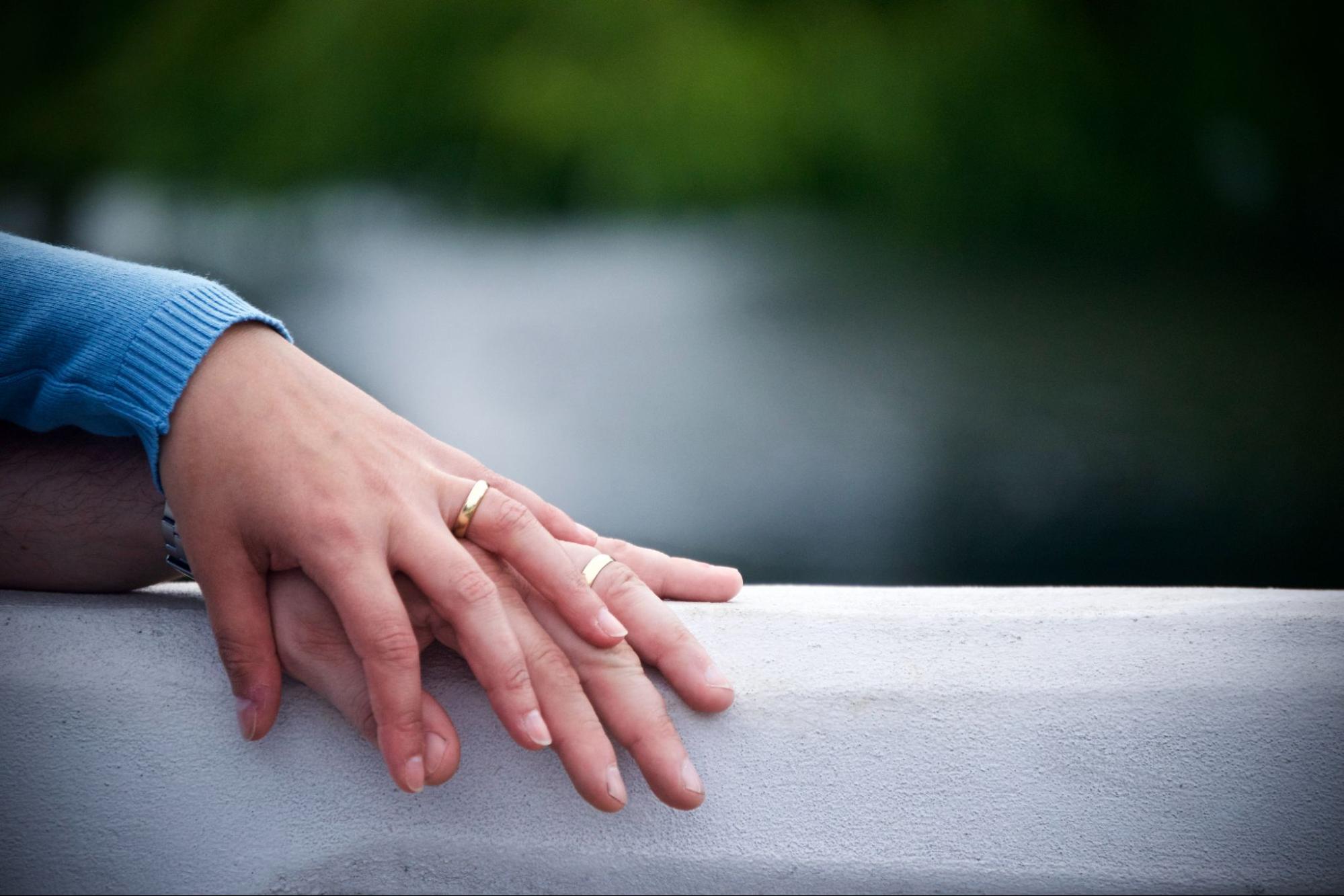 a married couple stack their hands on top of each other, showing off their matching wedding bands.