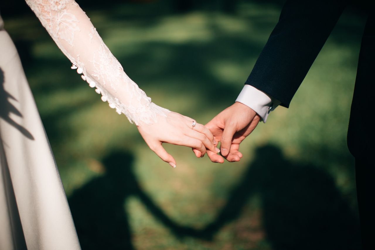 A bride and groom hold hands as they walk through a field.