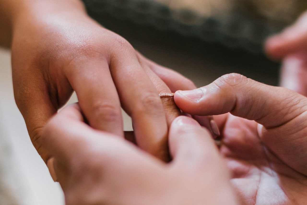 a groom slips a dainty diamond wedding band on his bride’s finger during their ceremony.