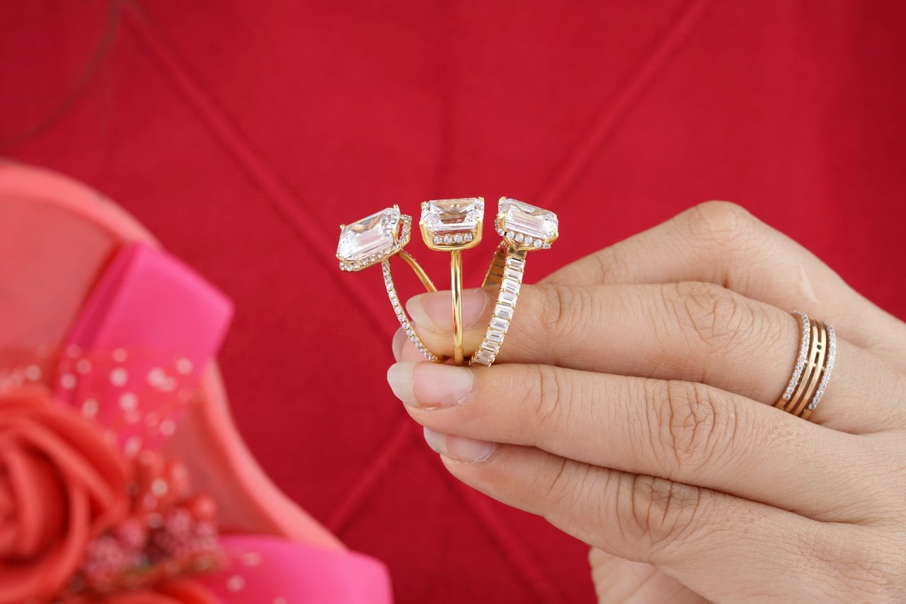 lady’s hand wearing a wedding band and holding three engagement rings