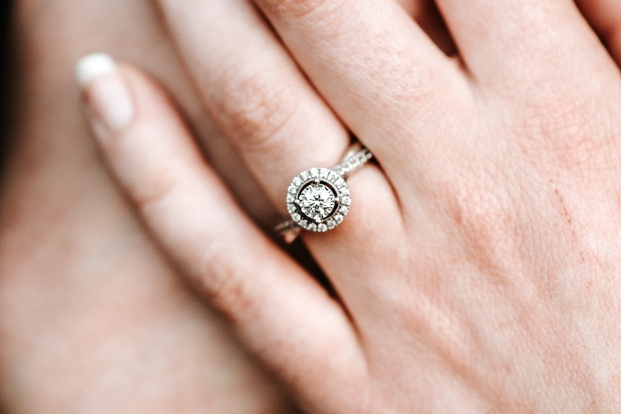 A closeup of a halo engagement ring with a twisting side stone shank on a woman’s hand.