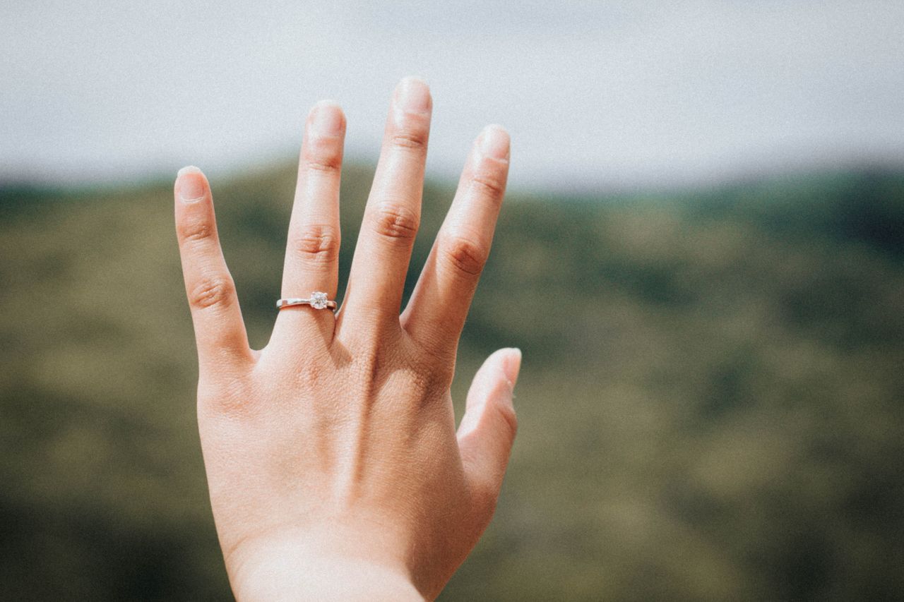 A woman wearing a gold solitaire engagement ring admires her ring outdoors.