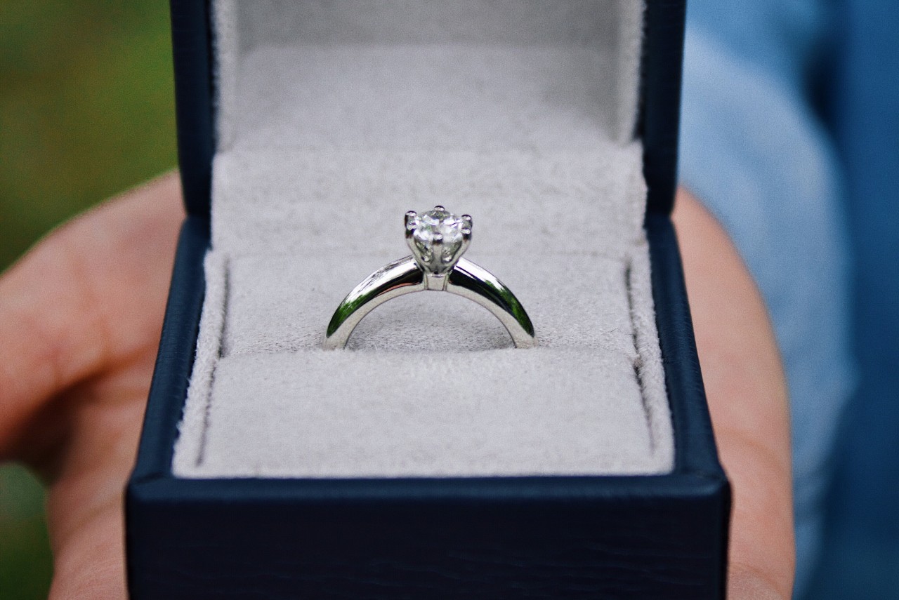 A man presents a platinum solitaire engagement ring in a black ring box.